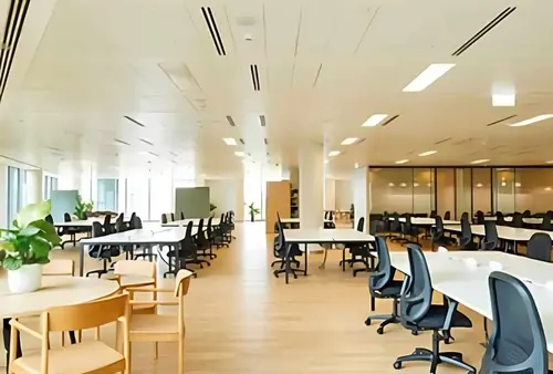 Open-plan office floor at 22 Sea Containers with rows of white bench desks, dark task chairs, a wooden table with chairs, a structural column and glazed partition offices.