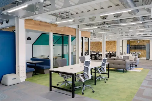 Desks and soft seating at 10 Parkway, on a green rug beneath the exposed ceiling